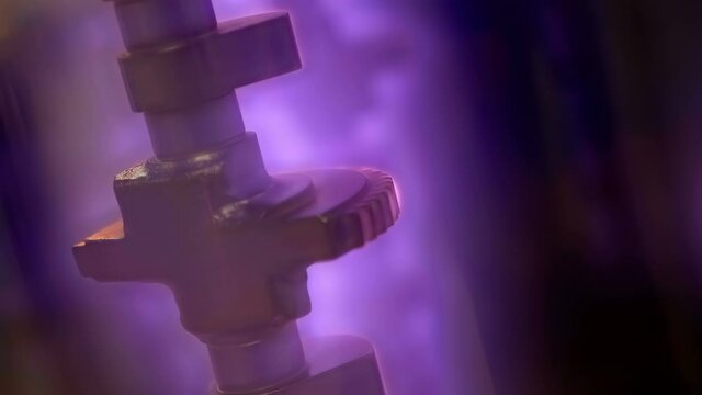 The camshaft of a car engine in a vacuum and a beautiful mesmerizing glow of the plasma that has formed around the object. Closeup