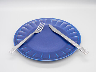 白い背景に置かれた紺色のお皿とカトラリー（ナイフ及びフォーク）