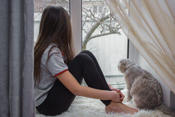 The child is resting on the windowsill and looking out the window with a lop-eared cat. Lazy...
