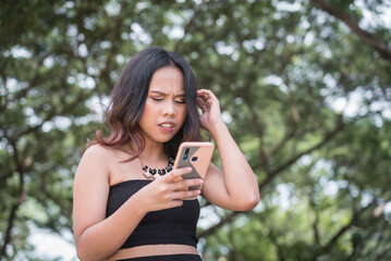 A worried young woman in a black top alarmed by a online bashing and harassment on her social media...