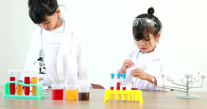 Little girl asian cute little student child learning research and doing a chemical experiment while making analyzing and mixing liquid in test tube at home on the table.