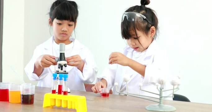 Little girl asian cute little student child learning research and doing a chemical experiment while making analyzing and mixing liquid in test tube at home on the table.