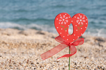 The heart on the beach is red from wood with a bow, a red ribbon. Holidays, love theme, congratulatory background.