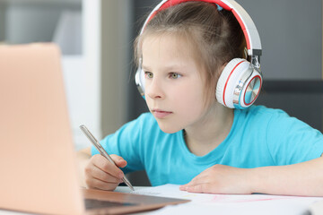 A girl in headphones looks attentively into a laptop