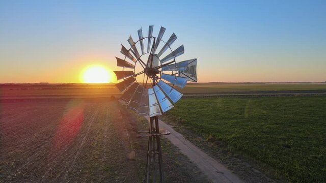 Motionless windpump starts to spin while drone orbiting around it. Closeup view during sunset