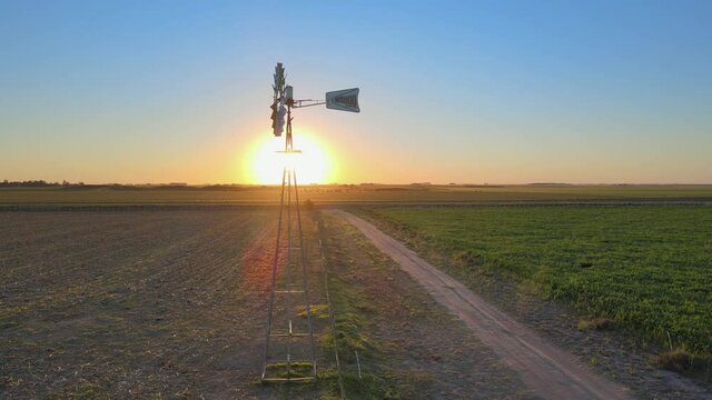Motionless rustic water pumping windmill. Aerial orbiting shot during sunset
