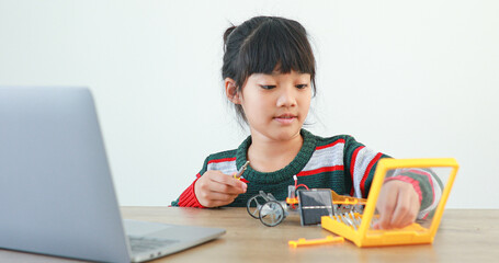 The little girl asian building robotic car in science lesson in the house . Which increases the development and enhances learning skills gifted brilliant children working with technology.