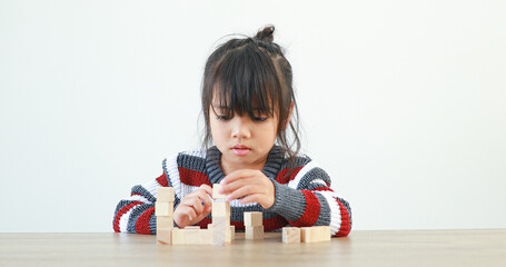 Naklejka premium The little girl playing with wooden building blocks Jenga. Having fun and learning creativity. Developing learning and enhancing skills smart kid concept.
