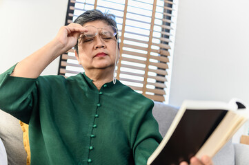 Senior people lifestyle health problem concept : Portrait photo of senior Asian woman has an eye long sighted problem trying to read message from book. Senior health care problem concept.