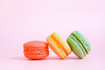 three colored sweet homemade macarons on sweet pink background, close up