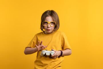 Child with gamepad playing video game. Little Girl 8-10 Years Old in Yellow T-shirt and Eyeglasses on Yellow Background. Schoolgirl fun, holds game controller with interest. Joystick in hands of kid © Vagengeim