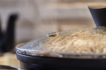 Frying pan lid with drops and steam close-up, in the kitchen