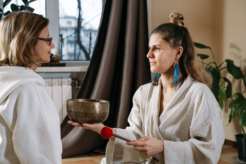 Sound healing with singing bowls, vibration massage and alternative therapy. Mental health care, meditation and relax. Therapist playing to old mature woman in 60s. singing, meditating practice