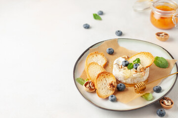 Traditional baked brie cheese or camembert with honey, nuts, blueberries and mint leaves, with breadcrumbs.