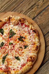 Uncut Italian pizza served with fresh basil leaf on Wooden board on dark texture background. Hot pizza with tomatoes and pesto sauce