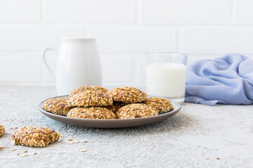 ceramic plate with oatmeal homemade cookies against the background of a white brick wall, a jug of milk and a filled glass. healthy breakfast.