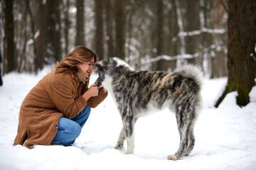 Love to the animals. Young woman playing in the snow with a husky dog.