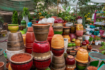 Several ceramic pots of different sizes and colors, next to ornamental plants and flowers inside a plant nursery.