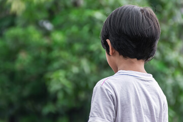 a cute and brave little boy standing on the park with the back view ready to play and having fun with beautiful green garden background