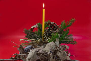 Orthodox Christmas decoration, burning candle in basket with pine tree, oak tree leaves, pine cone on red background