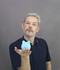 Middle age men with gray hair and beard showing piggy bank on gray background. Saving money concept.
