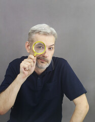 Middle age men with gray hair and beard looking through magnifying glass on gray background.