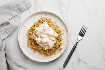 Bulgur with chicken and cream sauce. Dinner idea with bulgur porridge and chicken fillet. White background and white plate. Top view.