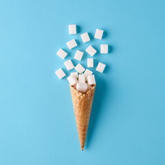 Sugar cubes on ice cream cone on blue background. Sweet food addiction and sugar diet for health