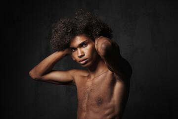 Shirtless black man with piercing holding his head and looking at camera