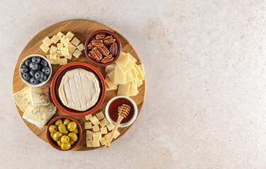 Top view of a tasty cheese board with berries, honey, nuts, olives, and cheese varieties on a circle kitchen plate. Gourmet food, copy space.