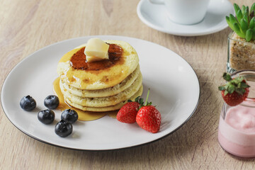 Pancakes served with butter, honey and fruirs served on a wooden table