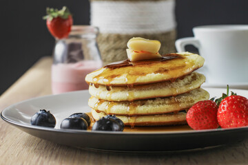Pancakes served with butter, honey and fruirs served on a wooden table