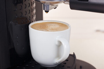 White cup of coffee under horn coffee maker.