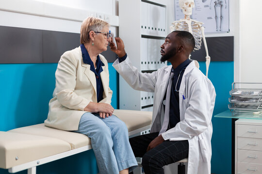 African american specialist doctor measuring temperature putting infrared thermometer on senior woman patient forehead discussing fever treatment. Medical appointment in hospital office
