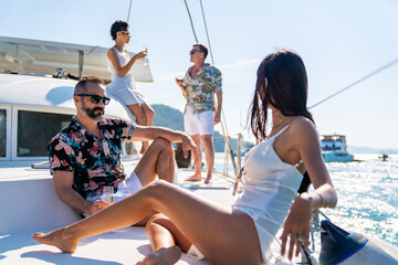 Group of Caucasian people friends enjoy luxury party drinking champagne together while catamaran boat sailing in the ocean. Man and woman relax outdoor lifestyle sail yacht on tropical travel vacation