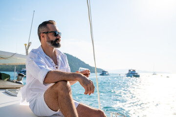 Caucasian man enjoy outdoor luxury lifestyle with alcoholic drinks while catamaran boat sailing at summer sunset. Handsome male relaxing outdoor leisure activity with tropical travel vacation trip - Powered by Adobe