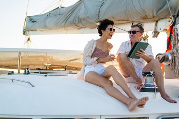 Caucasian businessman and businesswoman working outdoor  together on digital tablet for online corporate business or stocks trading while luxury catamaran boat sailing on tropical summer vacation.