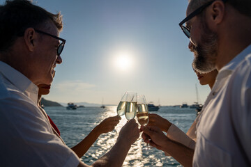 Group of man and woman friends enjoy party drinking champagne with talking together while catamaran boat sailing at summer sunset. Male and female relax outdoor lifestyle on tropical travel vacation