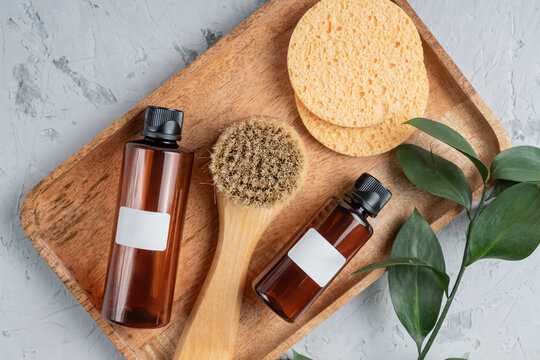 Fsce and body care spa treatment consept. Two brown unbranded bottles, face brush and sponges on wooden tray. Unbranded packaging. Mockup