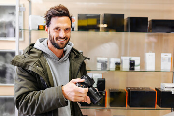 Happy young customer holding camera in store