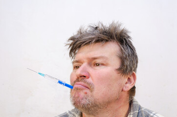 Portrait of a weirdo holding a blue syringe in his mouth.