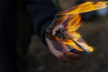 Close-up of a man's hand holding a burning sheet of paper. Sheet