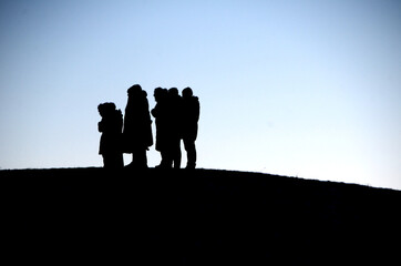 Silhouettes of people standing in a group at the top of a hill