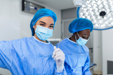 Portrait of female woman nurse surgeon OR staff member dressed in surgical scrubs gown mask and hair net in hospital operating room theater making eye contact smiling pleased happy looking at camera