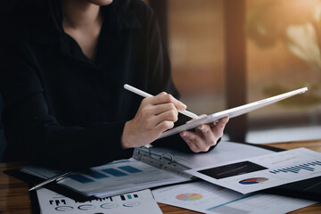 Electronic work concept, female employee is using tablet and ducument to analyze company profits to...