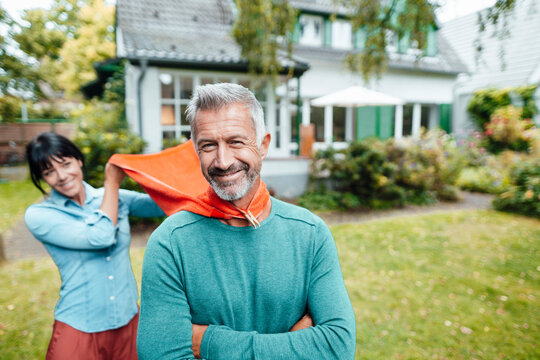 Woman holding scarf of man with arms crossed in backyard