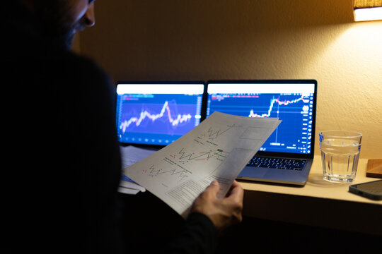 Businessman reviewing documents trading cryptocurrency on laptop at home office