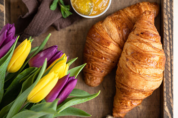 Romantic breakfast with crispy croissants, jam, chocolate cream, coffee and colorful tulips on old wooden tray. Top view.