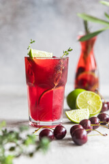 Lemonade or non-alcohol cocktail with cherry and lime, grey concrete background. Summer refreshment drink.