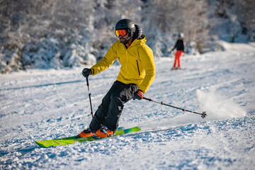 Fototapeta na wymiar Young person in fashionable clothes is skiing past the camera on a ski slope on a sunny day. Carve or carving on ski piste, perfect weather, strong backlight.